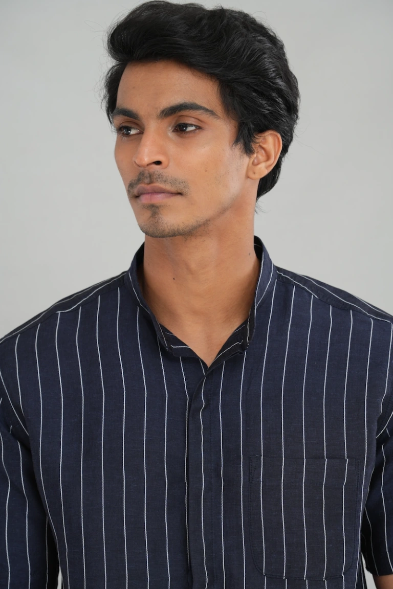 A model wearing a navy blue striped linen cotton mixed shirt with short sleeves, a chest pocket, and a relaxed fit, ideal for casual summer outings or refined everyday styling.