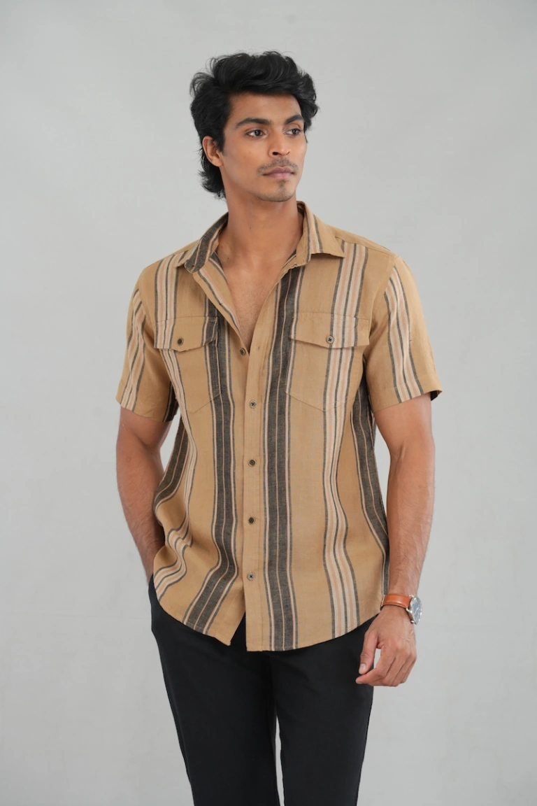 A model wearing a Desert Stripes Linen shirt with buttoned chest pockets, featuring bold beige and black vertical stripes, perfect for casual summer wear or stylish everyday outfits.