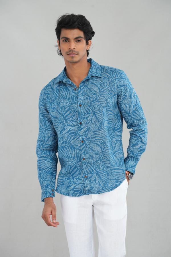 Model wearing a linen long-sleeve blue shirt with an intricate leaf pattern, button-down design, and tailored fit, paired with white trousers for a casual and breathable look