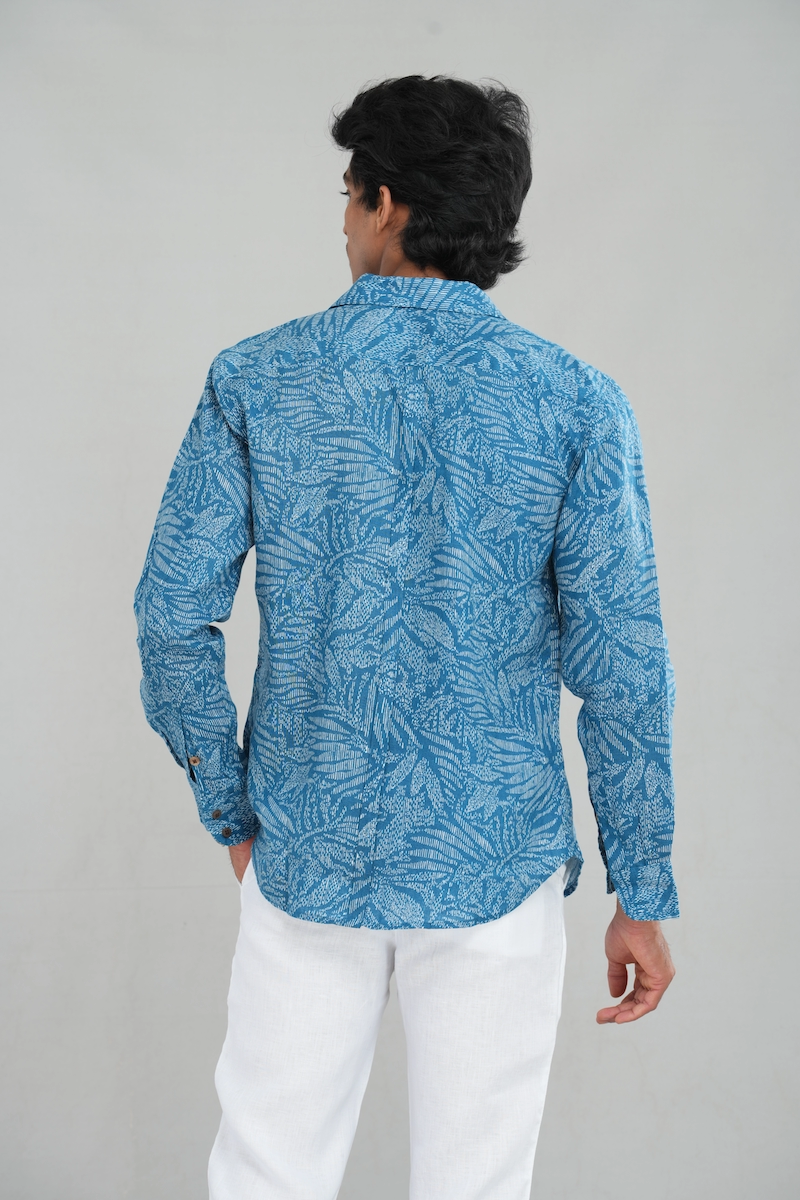 Model wearing a linen long-sleeve blue shirt with an intricate leaf pattern, button-down design, and tailored fit, paired with white trousers for a casual and breathable look