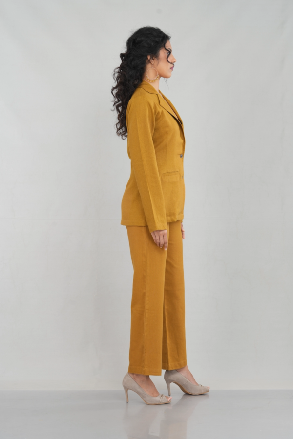 A stylish woman wearing a goldenrod oversized two-button blazer made of linen cotton blend, featuring a sleek lapel design and practical front pockets, paired with matching trousers.