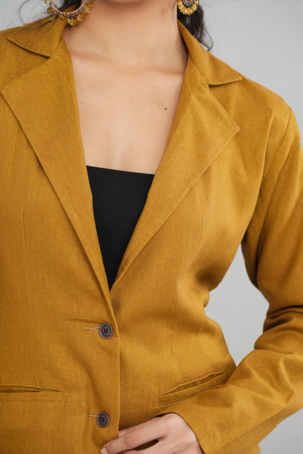 A stylish woman wearing a goldenrod oversized two-button blazer made of linen cotton blend, featuring a sleek lapel design and practical front pockets, paired with matching trousers.