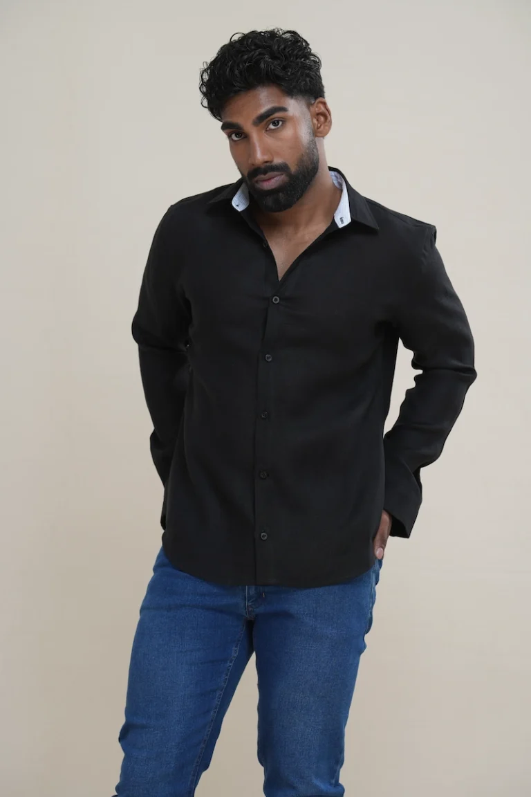 Man wearing a black tonal linen shirt featuring a white stripe contrast inner collar and black buttons, paired with blue jeans.