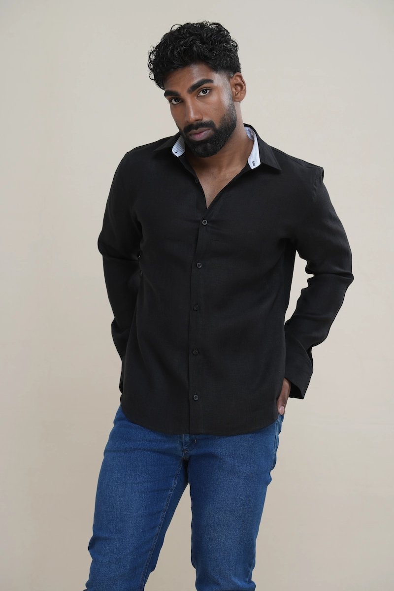 Man wearing a black tonal linen shirt featuring a white stripe contrast inner collar and black buttons, paired with blue jeans.