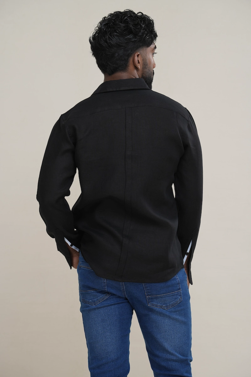 Man wearing a black tonal linen shirt featuring a white stripe contrast inner collar and black buttons, paired with blue jeans.
