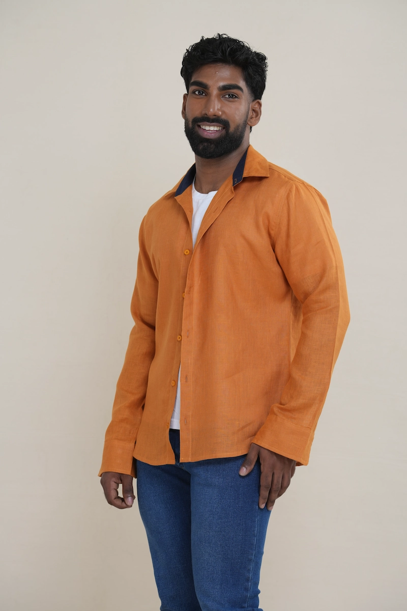 Man wearing a terracotta brown long sleeve linen shirt with a navy contrast inner collar, styled open over a white t-shirt and jeans. Man smiling while wearing a terracotta brown long sleeve shirt featuring a navy blue contrast collar.