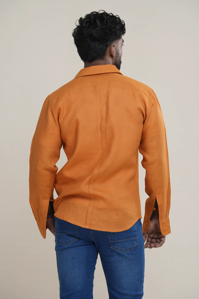 Man wearing a terracotta brown long sleeve linen shirt with a navy contrast inner collar, styled open over a white t-shirt and jeans. Man smiling while wearing a terracotta brown long sleeve shirt featuring a navy blue contrast collar.