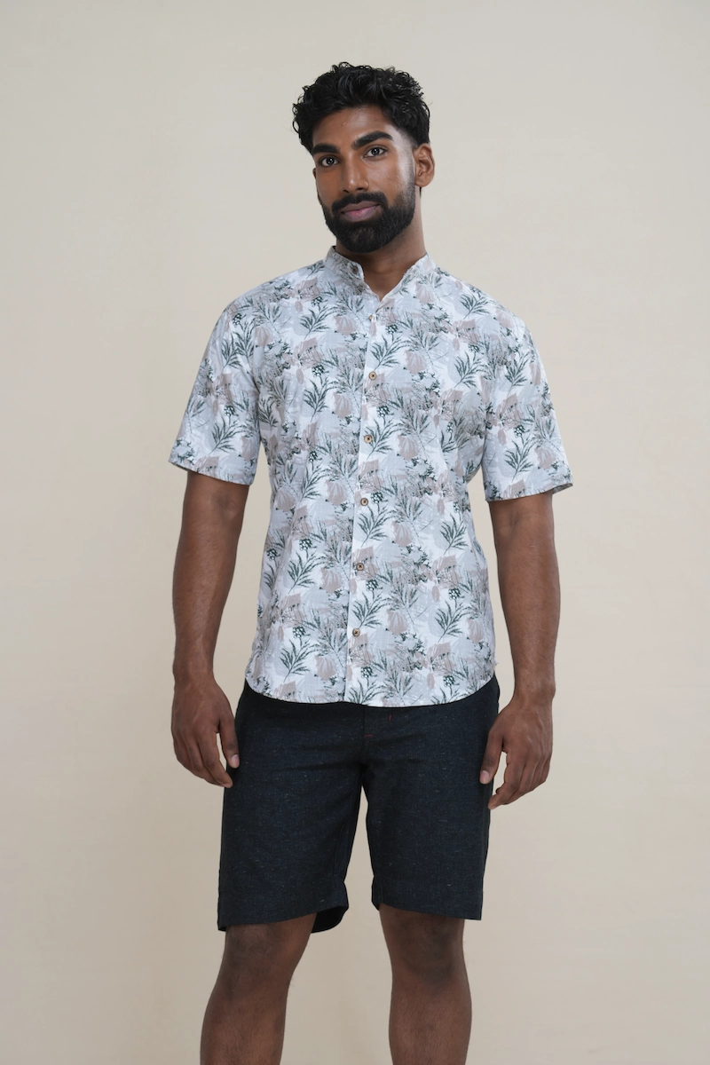 Close-up of a men's cotton Mandarin collar short sleeve shirt with a light grey base and green botanical print, featuring coconut buttons.