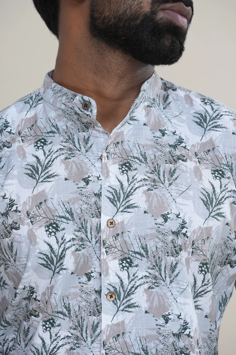 Close-up of a men's cotton Mandarin collar short sleeve shirt with a light grey base and green botanical print, featuring coconut buttons.