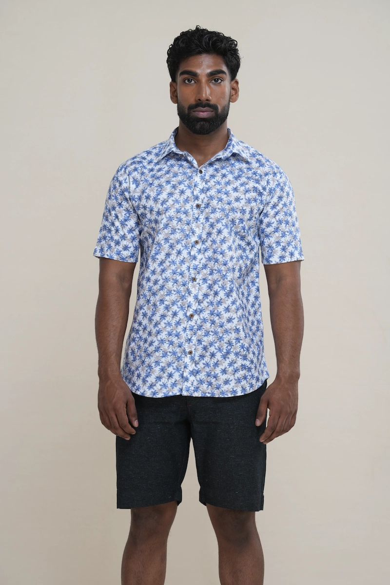 Man wearing a white cotton short sleeve shirt with a white and blue palm tree print, classic collar, and coconut buttons