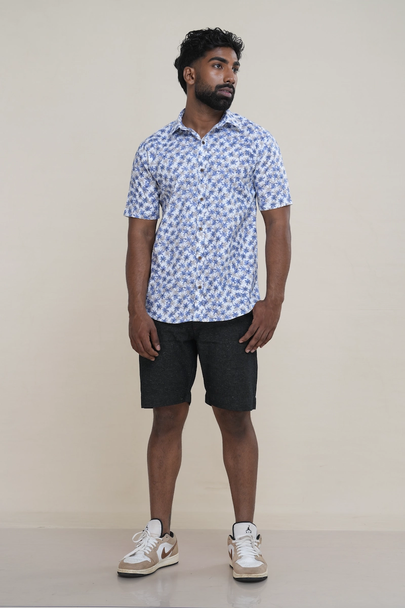 Man wearing a white cotton short sleeve shirt with a white and blue palm tree print, classic collar, and coconut buttons