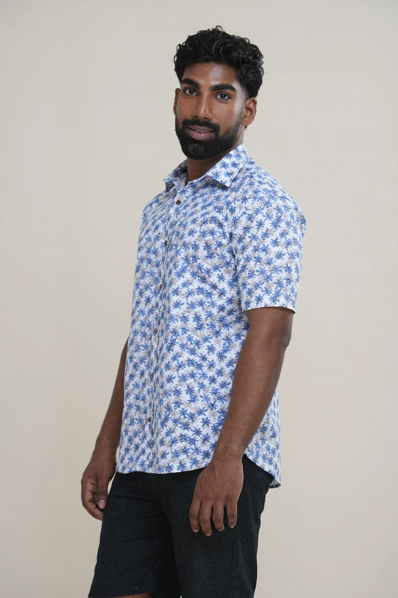 Man wearing a white cotton short sleeve shirt with a white and blue palm tree print, classic collar, and coconut buttons