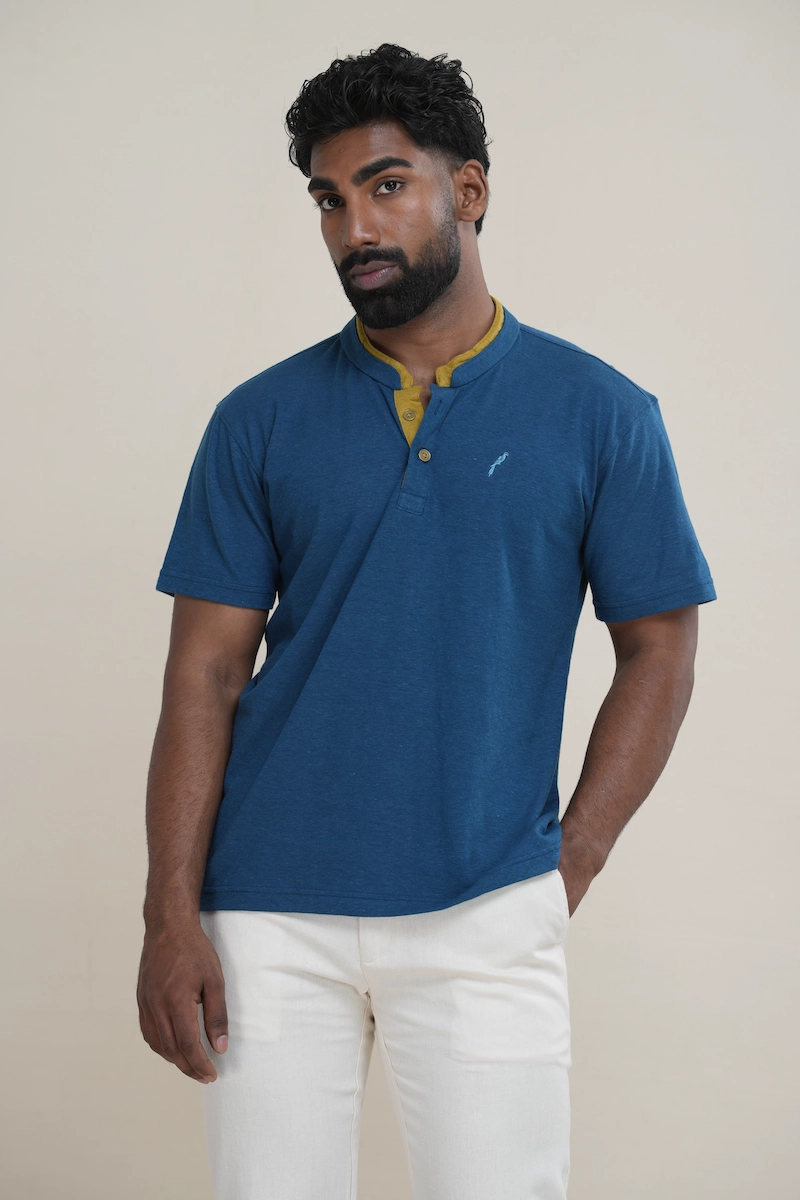 Close-up of a men's heathered deep turquoise cotton jersey layered collar Henley shirt with yellow-green inner collar detail, two buttons, and an embroidered parrot logo.
