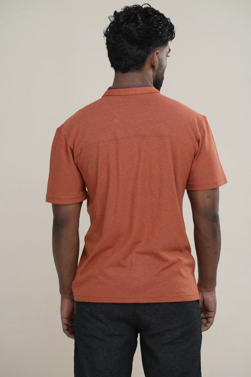 Man wearing a heathered terracotta orange cotton jersey Henley shirt with a layered double collar, two-button placket, and embroidered parrot logo