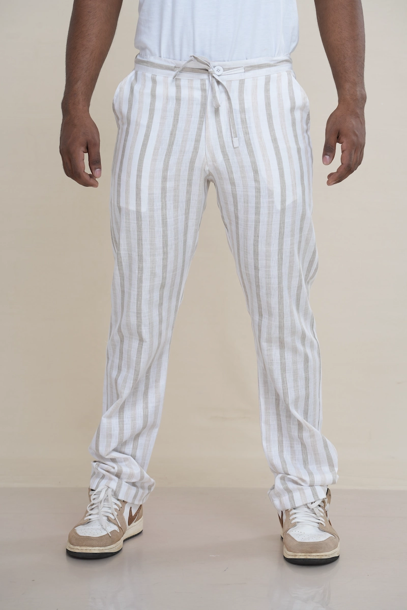 Man wearing off-white and beige striped linen drawstring trousers with a relaxed fit.Close-up of the waist of striped linen trousers, showing the drawstring tie and button closure detail.