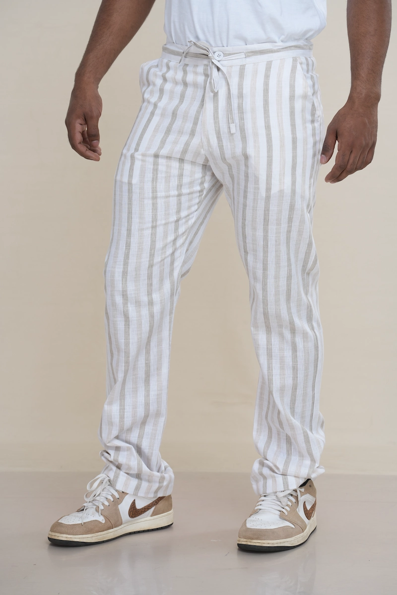 Man wearing off-white and beige striped linen drawstring trousers with a relaxed fit.Close-up of the waist of striped linen trousers, showing the drawstring tie and button closure detail.