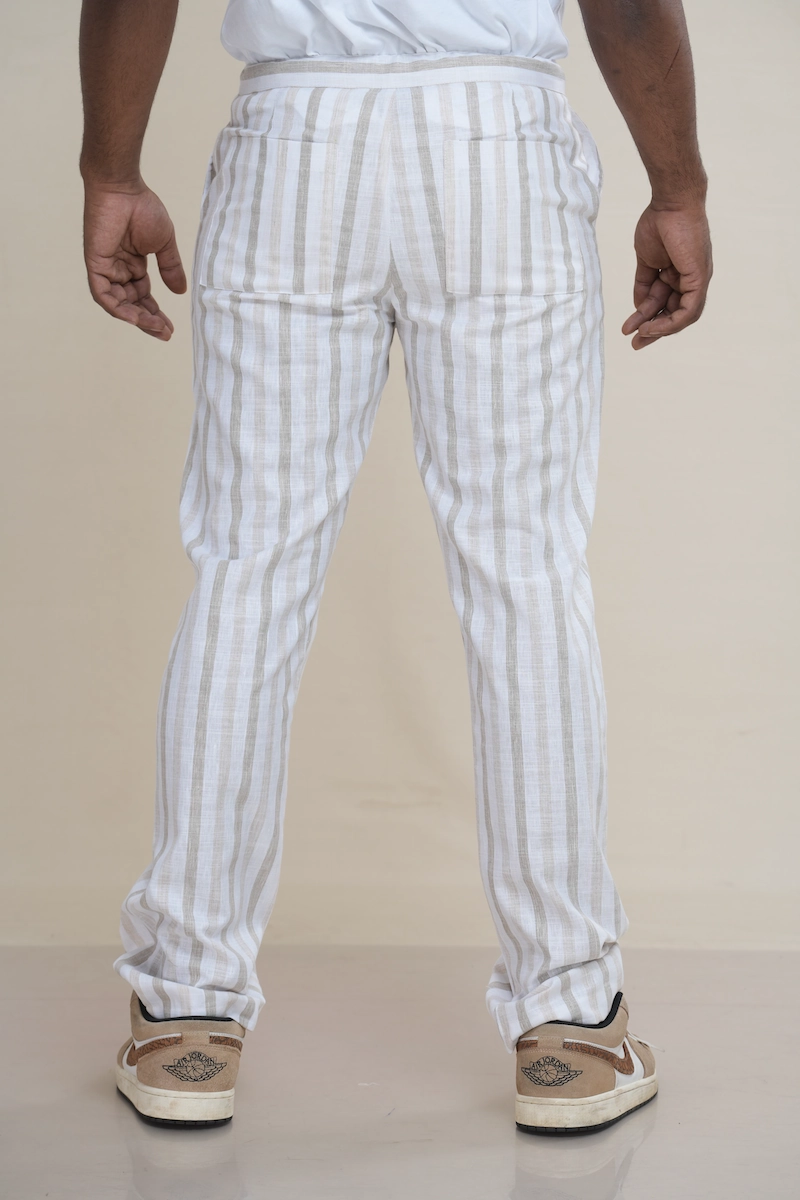 Man wearing off-white and beige striped linen drawstring trousers with a relaxed fit.Close-up of the waist of striped linen trousers, showing the drawstring tie and button closure detail.