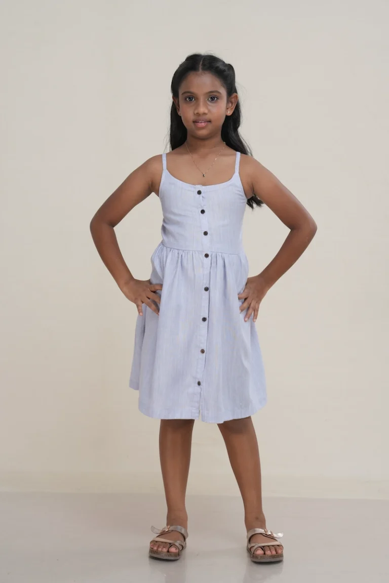 Young girl wearing a chambray blue linen button-front cami dress with adjustable straps.