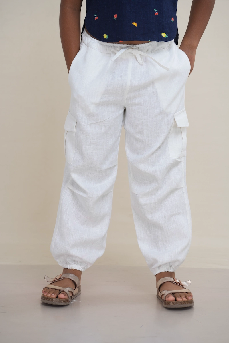 Young girl wearing classic white linen cargo jogger pants with an elasticated drawstring waist and side cargo pockets.