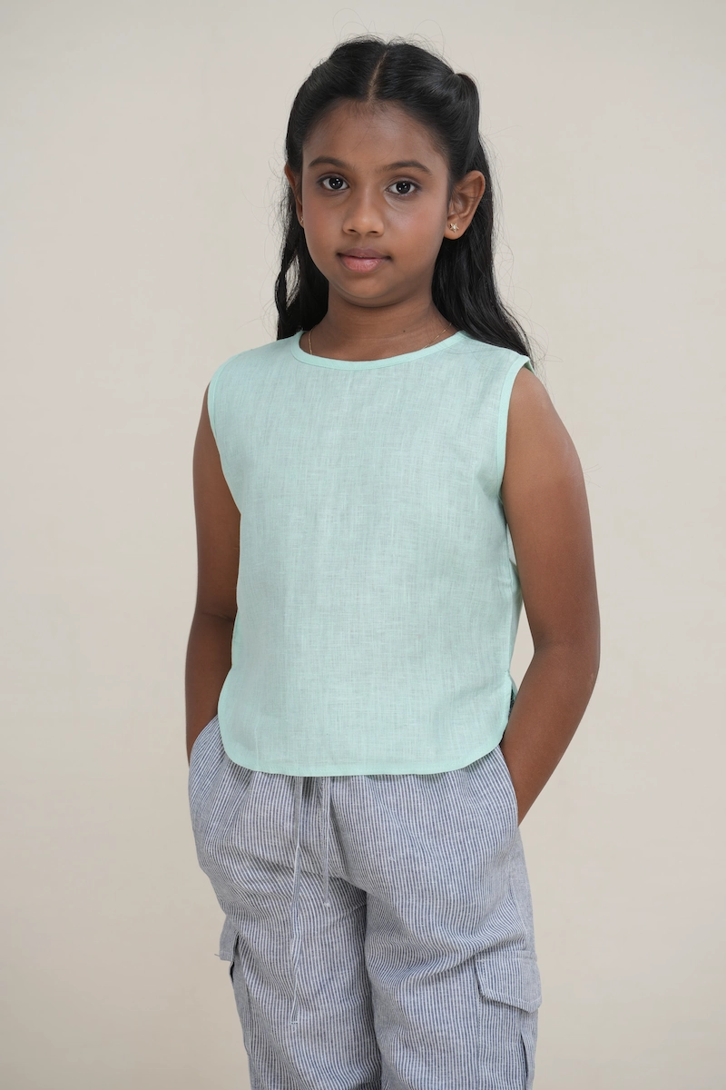 Young girl wearing a mint green linen sleeveless top with a button-back keyhole detail.