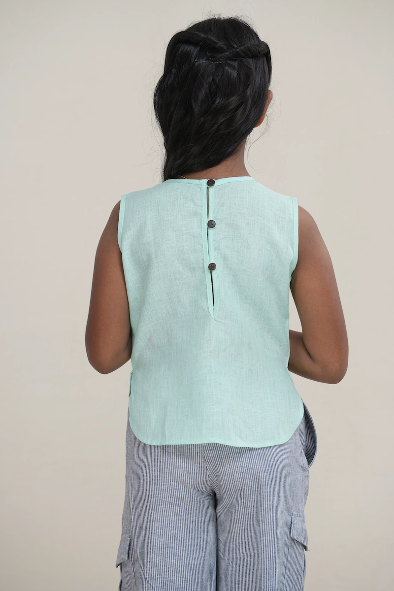Young girl wearing a mint green linen sleeveless top with a button-back keyhole detail.