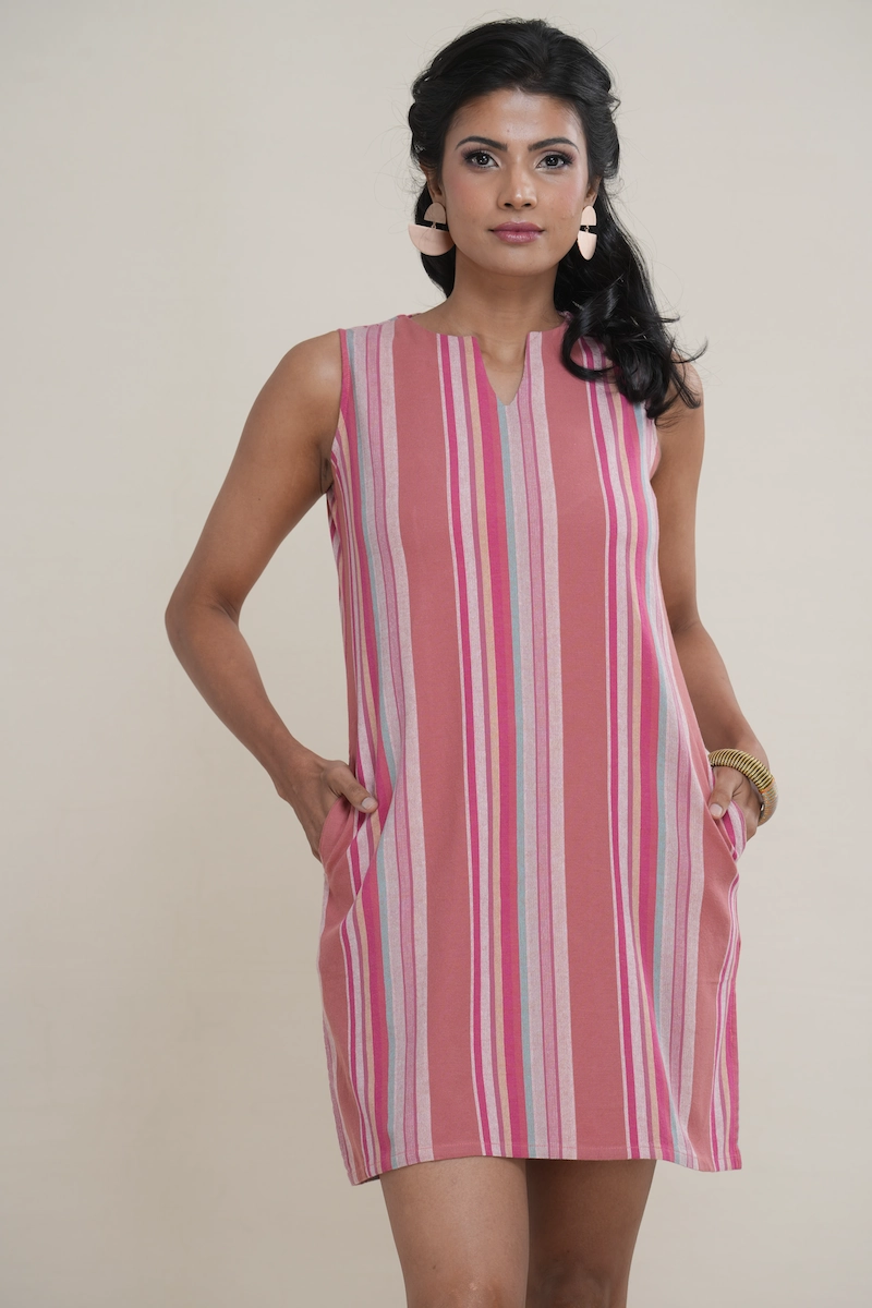 Woman wearing a dusty rose multi-color striped cotton shift dress, featuring a notch neckline, side pockets, and side slits.