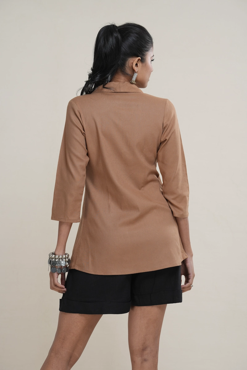 Woman wearing a caramel brown linen-cotton blend shawl collar tunic with an empire waist and three-quarter sleeves.