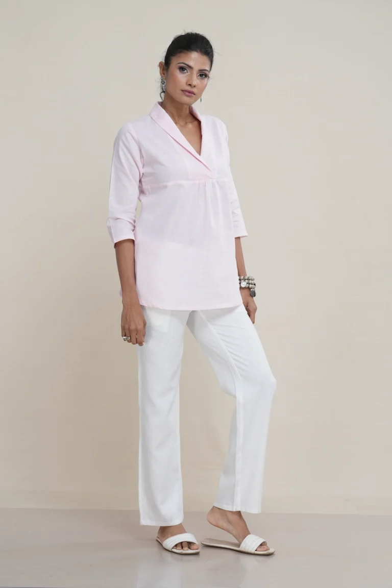 Woman wearing a pastel pink linen-Cotton blend shawl collar tunic top with an empire waist and three-quarter sleeves, the elegant shawl collar and empire waist detail on a pastel pink linen tunic top.