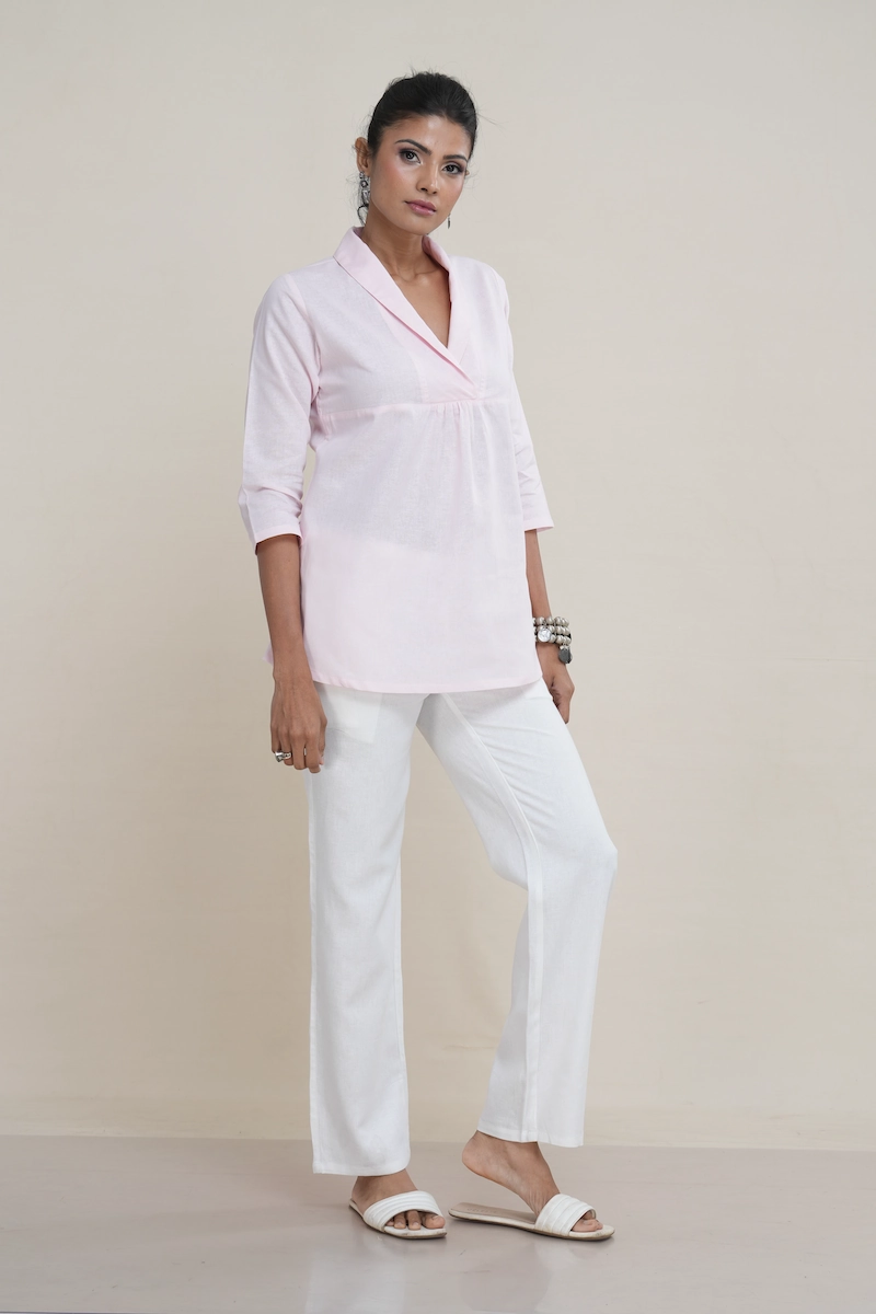 Woman wearing a pastel pink linen-Cotton blend shawl collar tunic top with an empire waist and three-quarter sleeves, the elegant shawl collar and empire waist detail on a pastel pink linen tunic top.