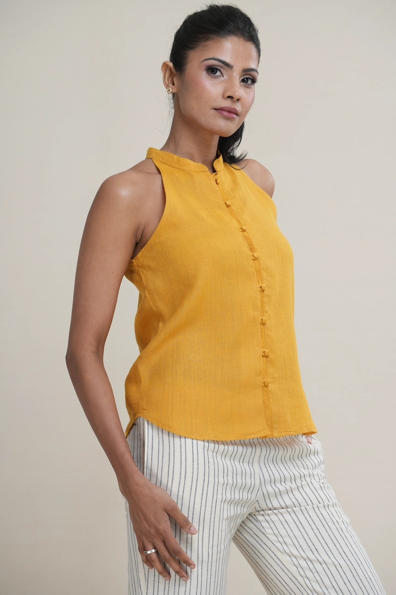 Woman wearing a mustard yellow linen Mandarin collar halter top with matching fabric-covered buttons.