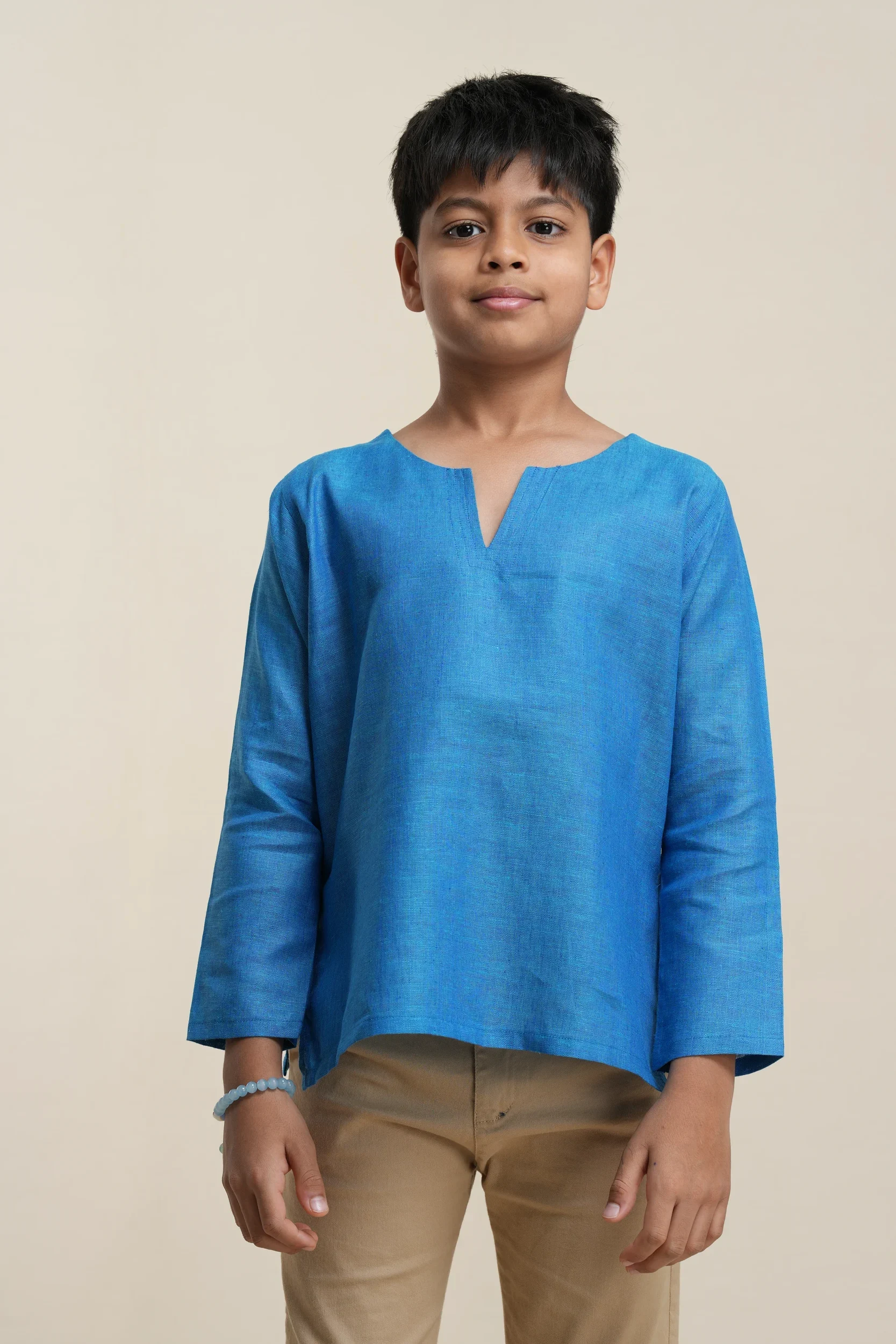 Boys long sleeve linen kurta in cerulean blue with v-notch neckline, paired with beige trousers, front view on model