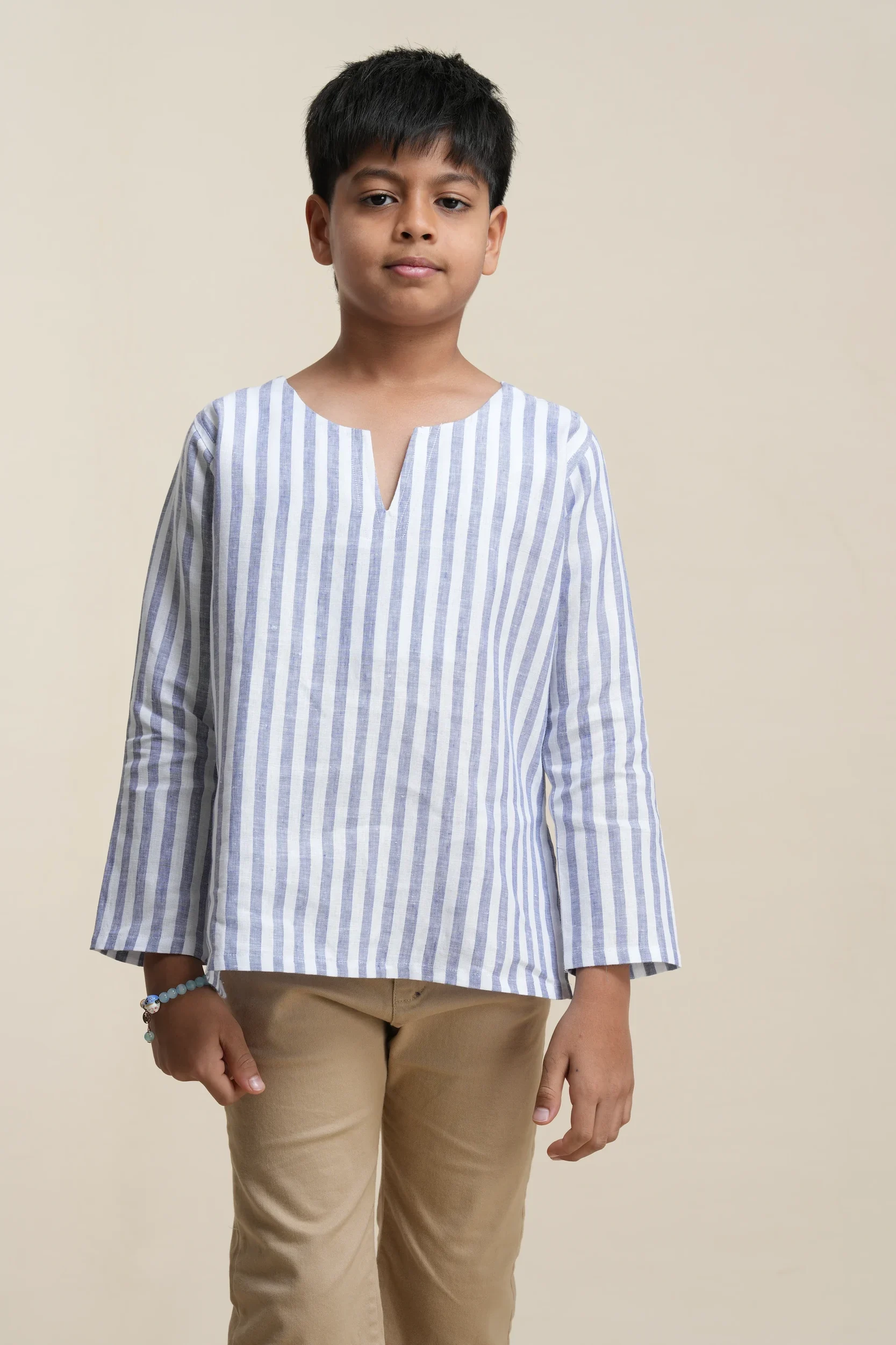 Young boy wearing blue and white striped linen kurta with long sleeves, v-notch neckline, paired with beige trousers