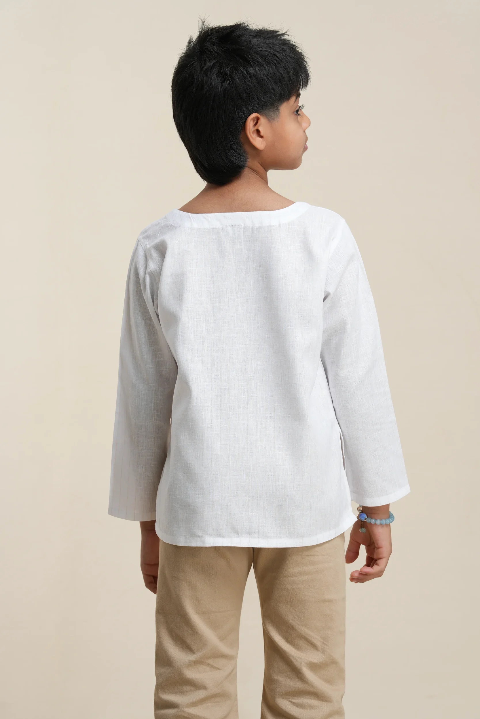 Back view of boys' white tonal stripe linen kurta with long sleeves, paired with beige trousers on neutral background