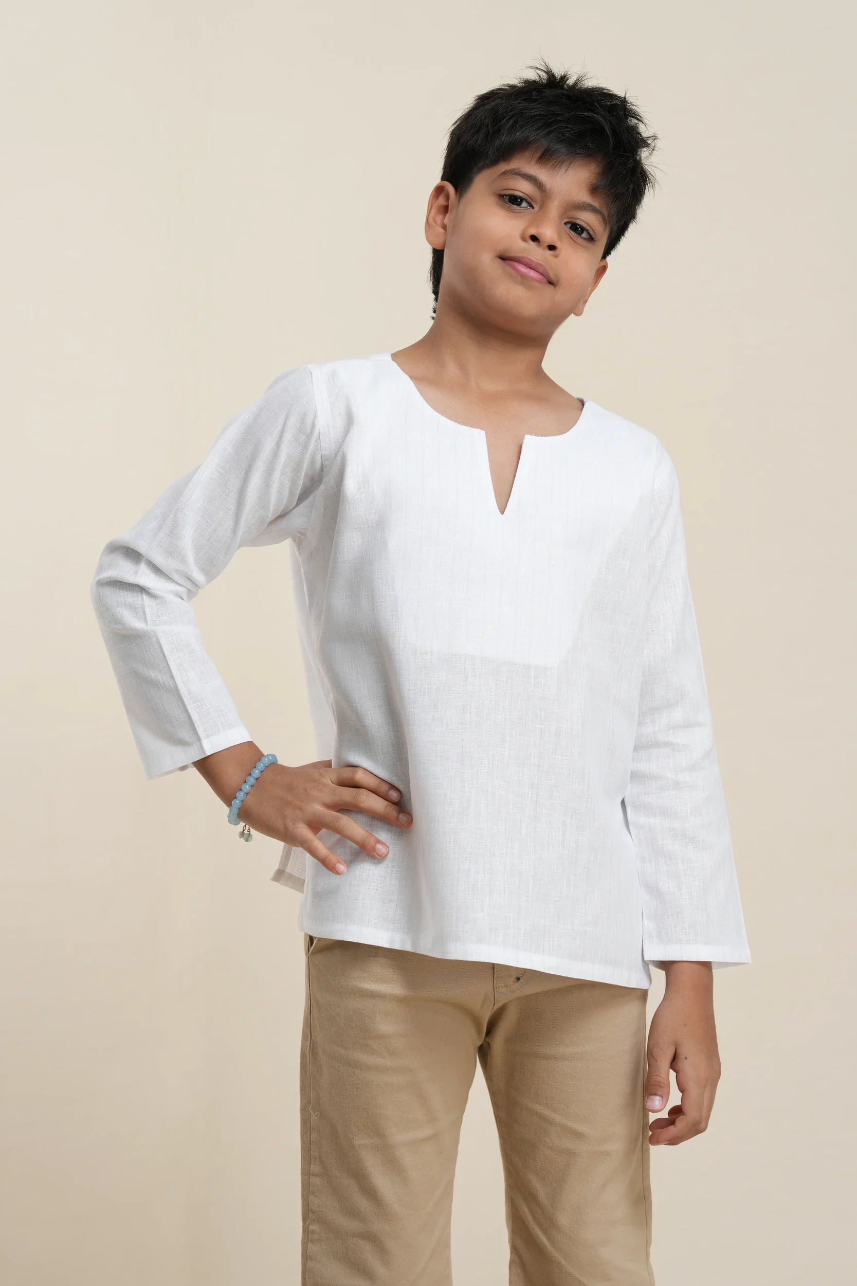 Young boy modeling white tonal stripe long sleeve linen kurta with notch neckline, paired with tan pants on beige background