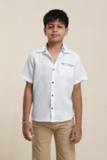 Young boy wearing white linen short sleeve shirt with blue floral collar detail, paired with beige trousers, front view