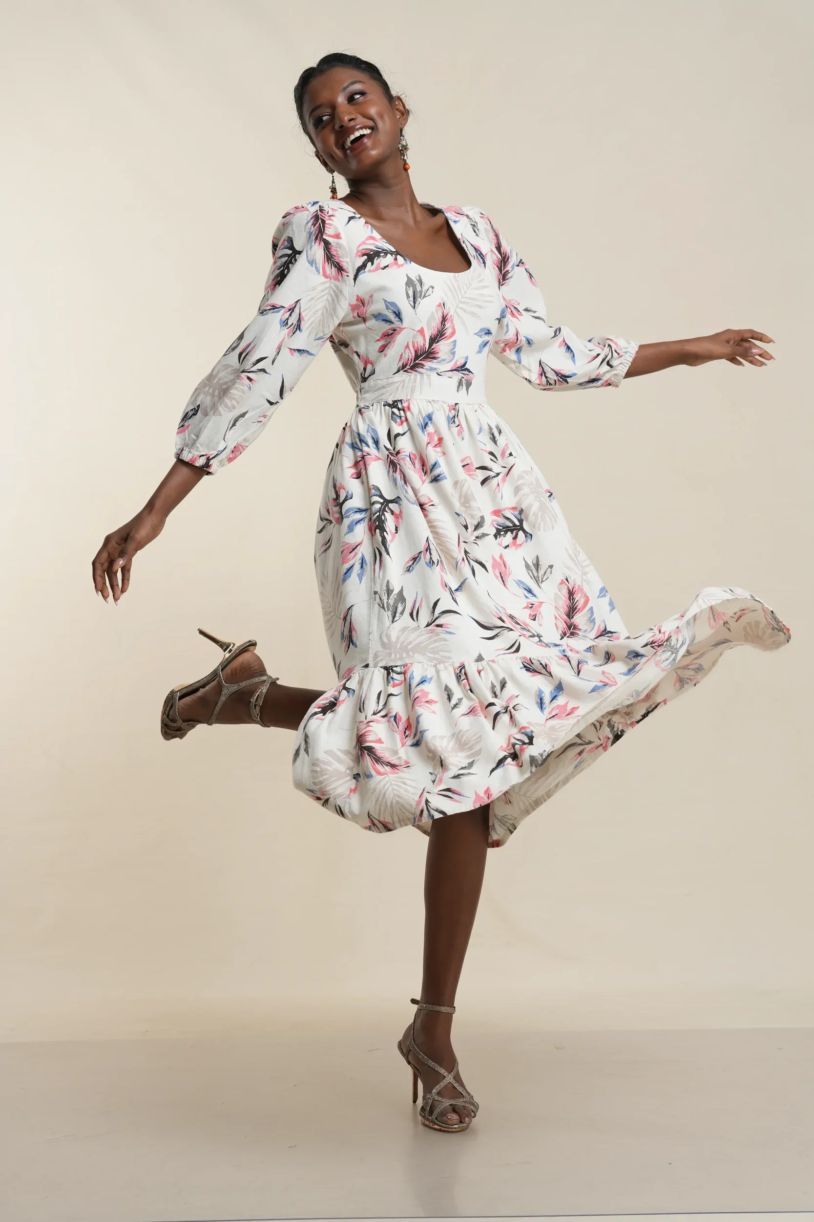 Woman in white botanical print tiered midi dress with floral pattern, 3/4 sleeves, cotton blend fabric, flowing skirt