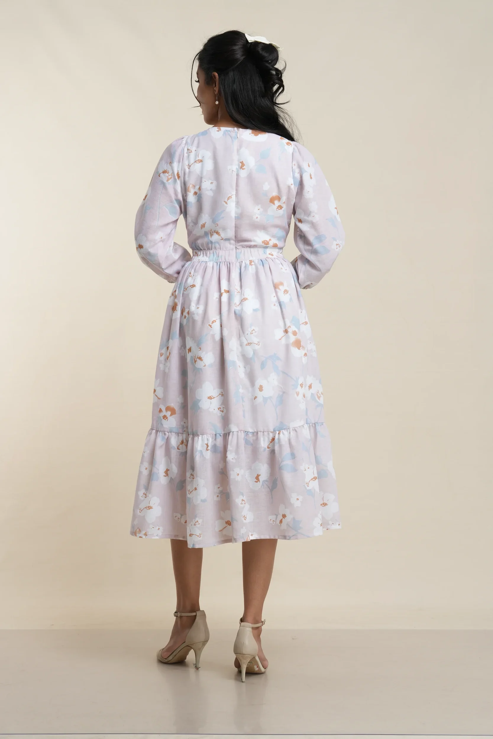 Back view of women's tiered midi dress in white and lilac floral print cotton blend, featuring gathered waist and ruffle hem