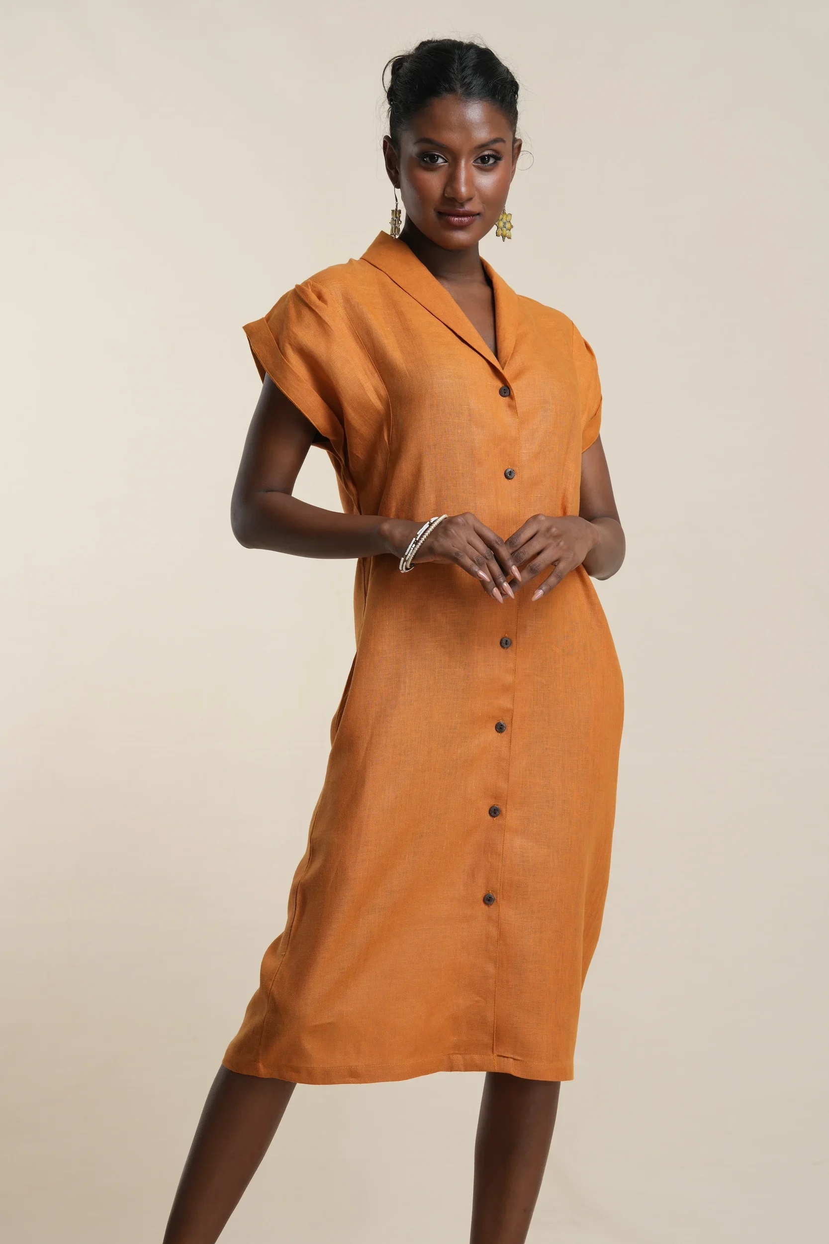 Model wearing rust orange linen button-front shirt dress with collar, short sleeves, and knee-length hemline