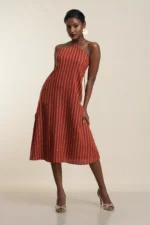 Rust striped halter neck midi dress in linen blend, front view on model with cream background, elegant A-line silhouette